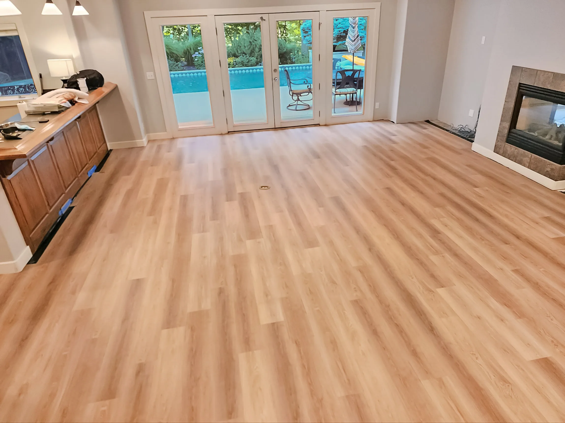 Light natural luxury vinyl plank flooring in a walkout lower level with French doors opening at ground level onto a pool patio