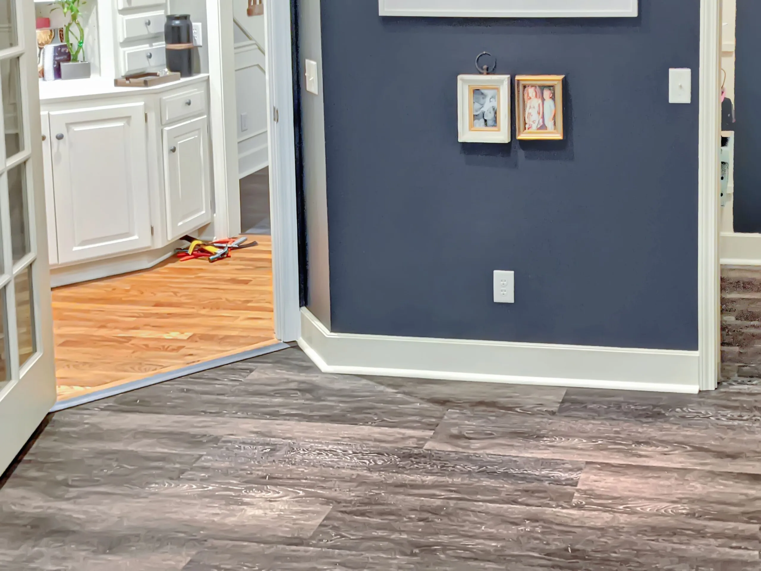 Luxury vinyl plank flooring meeting an existing hardwood floor at a doorway transition strip during an installation in Lenexa, Kansas