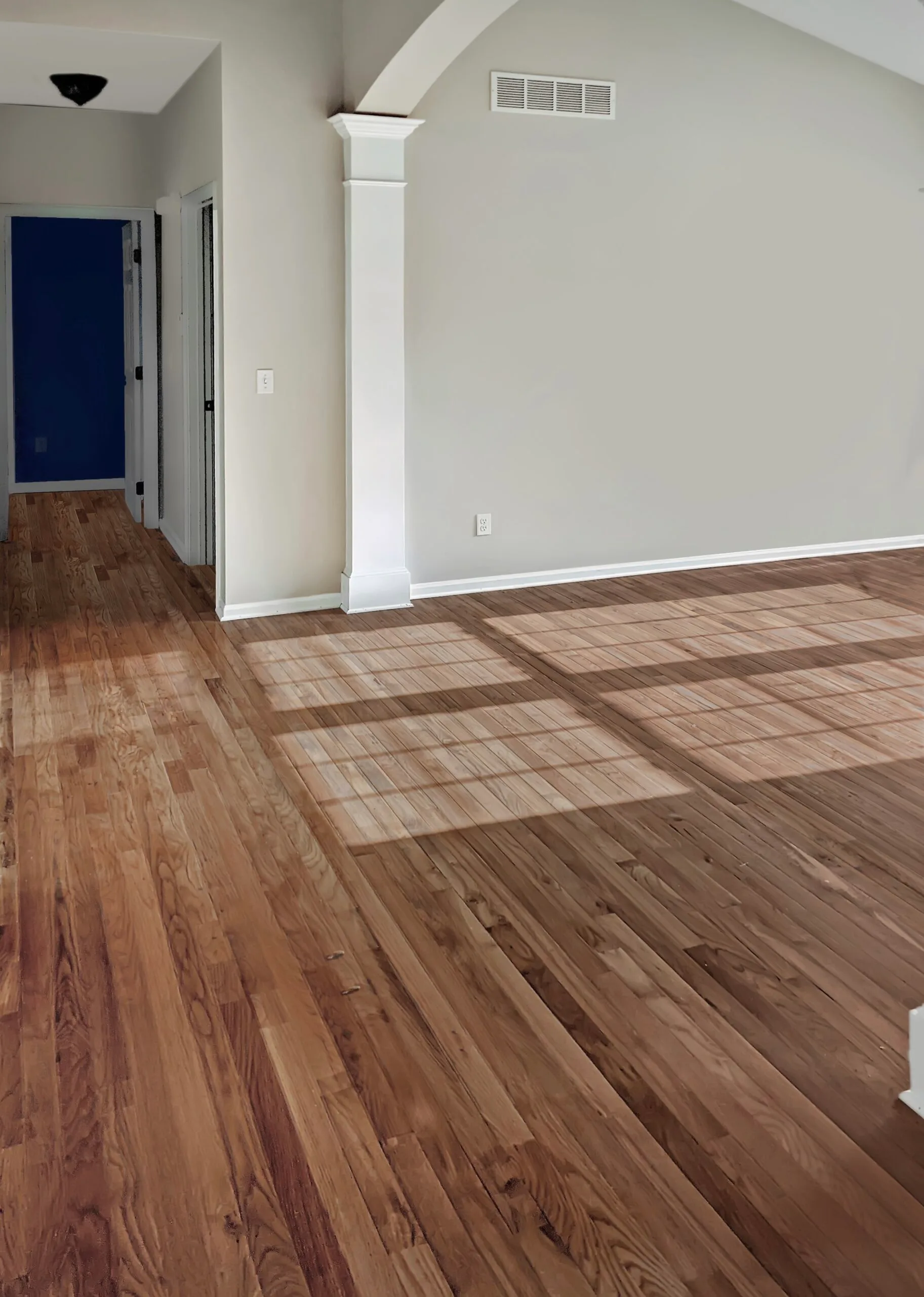 Freshly finished red oak hardwood flooring running from a hallway through an arched living room opening in an Overland Park, Kansas home