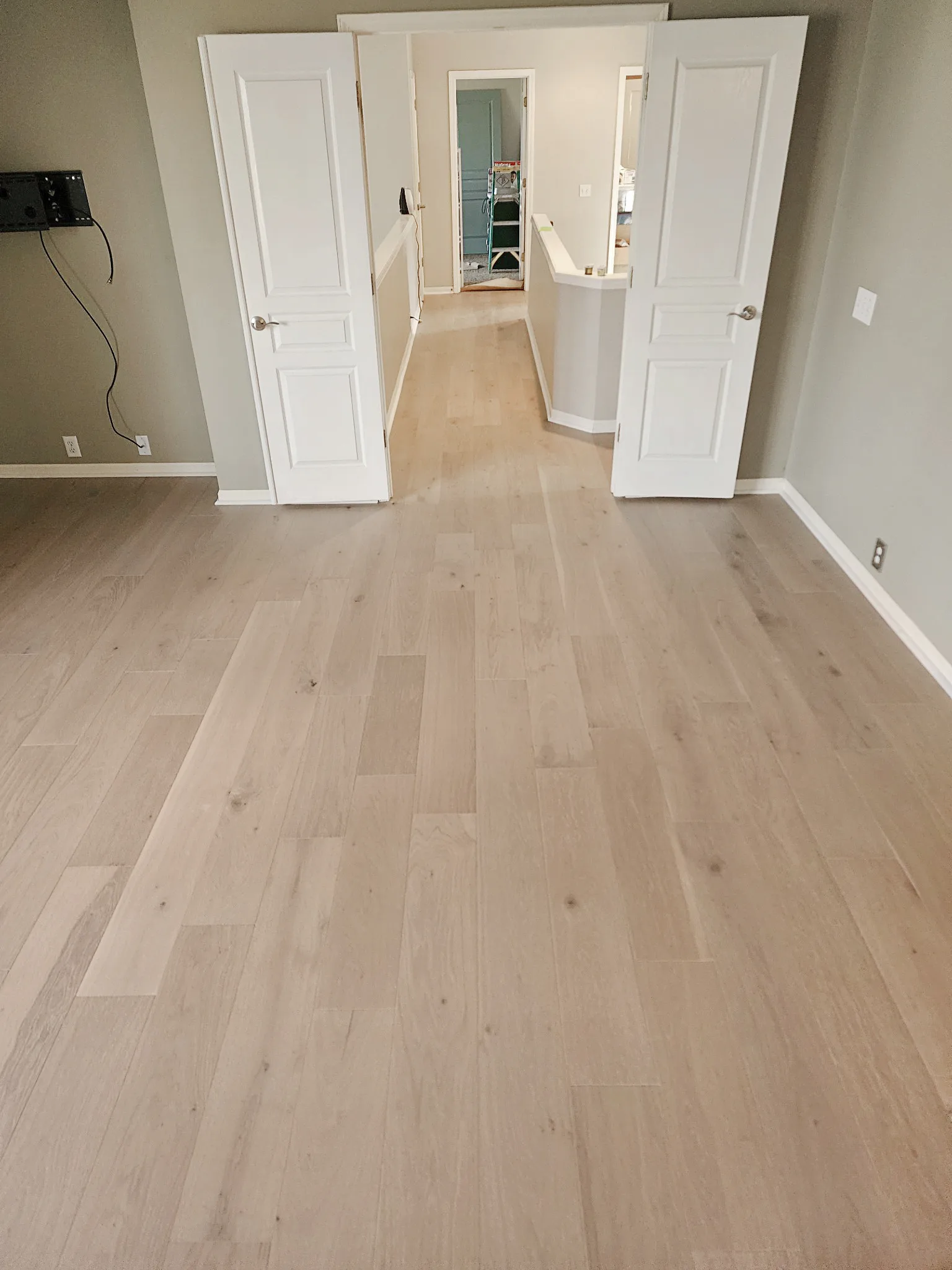 Light natural white oak hardwood flooring running continuously from a bedroom through open double doors into a hallway in an Overland Park, Kansas home