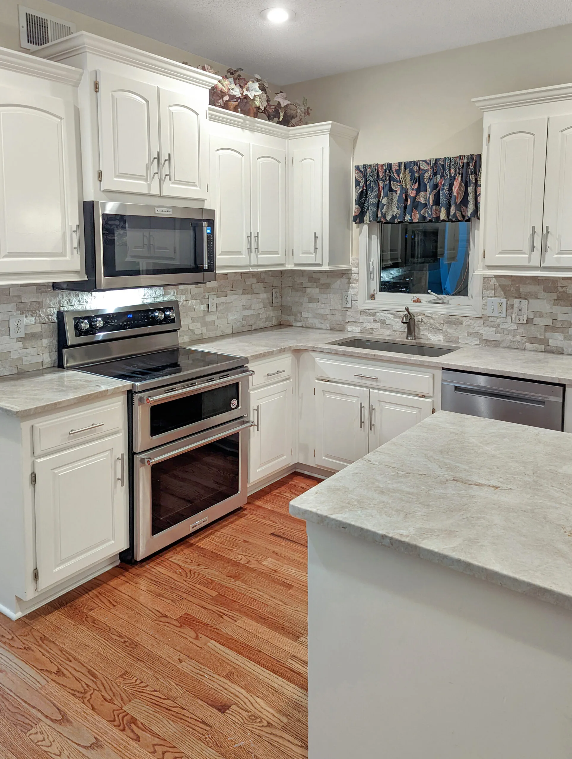 Red oak hardwood flooring carried into a white-cabinet kitchen with a stacked stone backsplash in Overland Park, Kansas