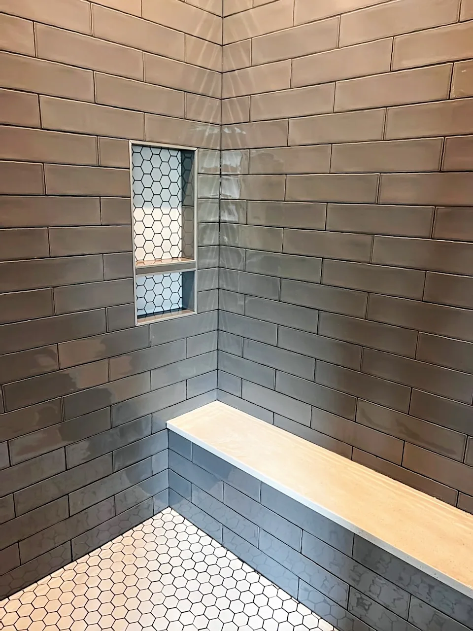 Grey subway tile shower walls with a recessed niche tiled in white hexagon mosaic, a stone bench and a white hexagon mosaic shower floor