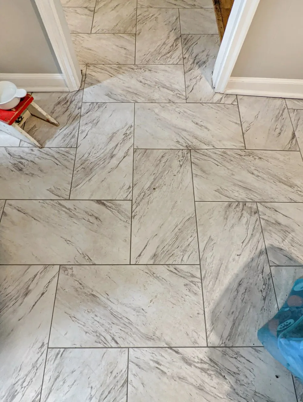 Large-format marble-look porcelain floor tile laid in an offset pattern through a bathroom doorway