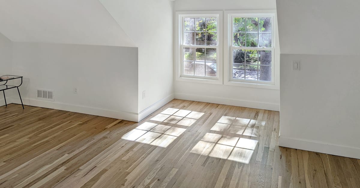 Newly installed natural oak hardwood floor in a sunlit upstairs room with sloped ceilings and a pair of windows in a Prairie Village home
